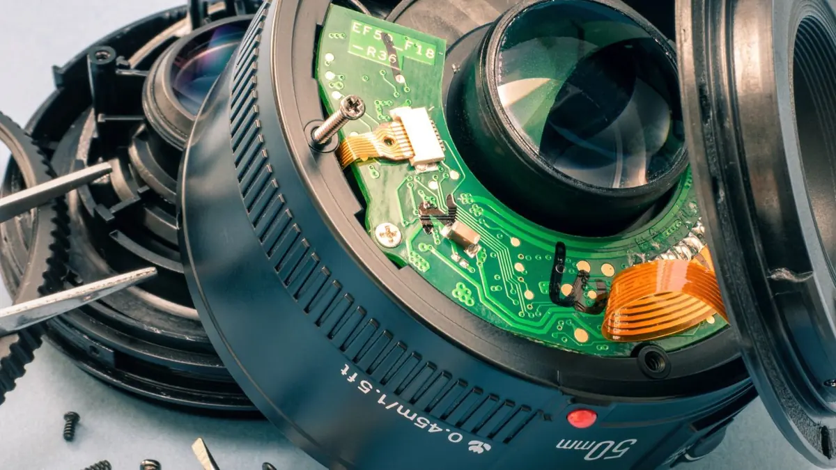 Išardytas fotoaparato objektyvas su matomais lęšių blokais ir autofokuso mechanizmu